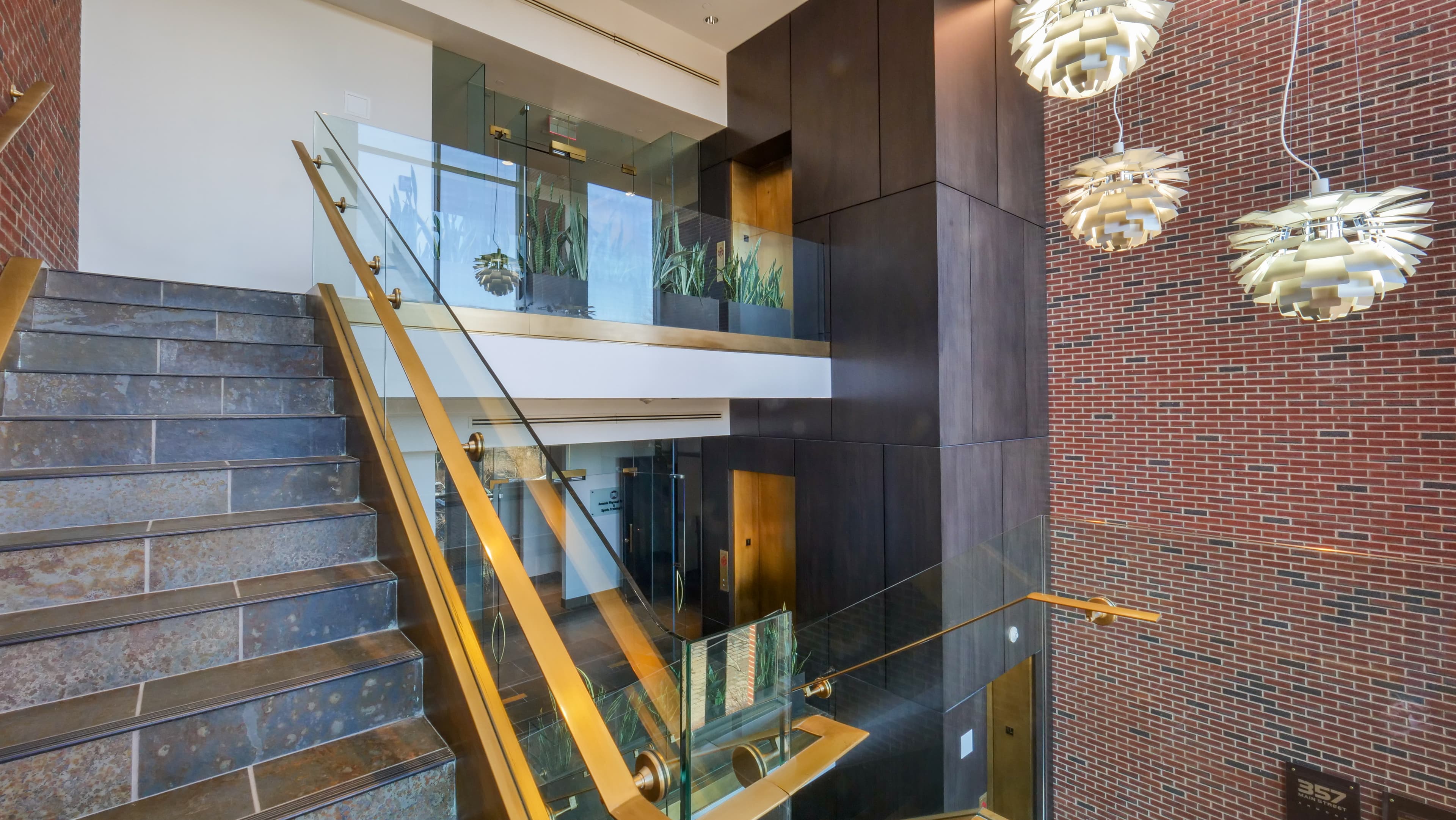 The double-height lobby with a brick feature wall, brass-railed stair, and sculptural pendant lighting.